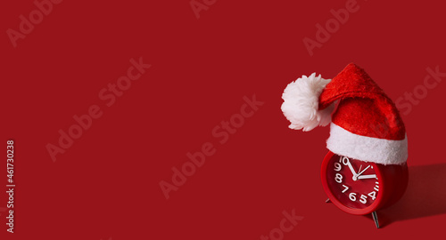 red alarm clock in red Christmas cap with white pompon on red background, koncept new year and christmas, fashionable minimalism, free space for text