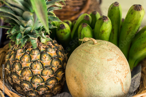 A pineapple, melon and green Lacatan banana in a basket, on display at a small fruit stand. photo