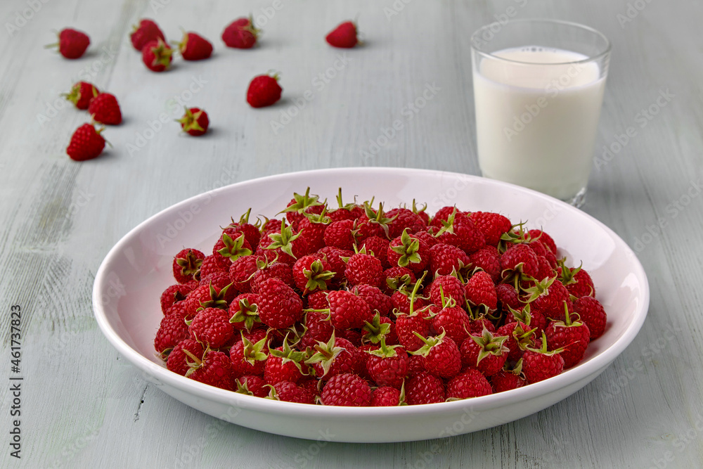 White plate with about ripe red raspberries and a glass of milk White plate with about ripe red raspberries and a glass of milk