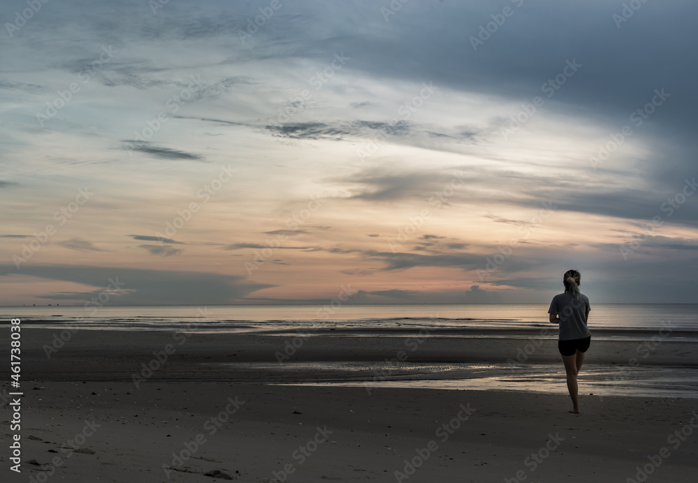 Young woman exercising on the sea beach at sunrise. Back view, Copy space, Focus and blur.