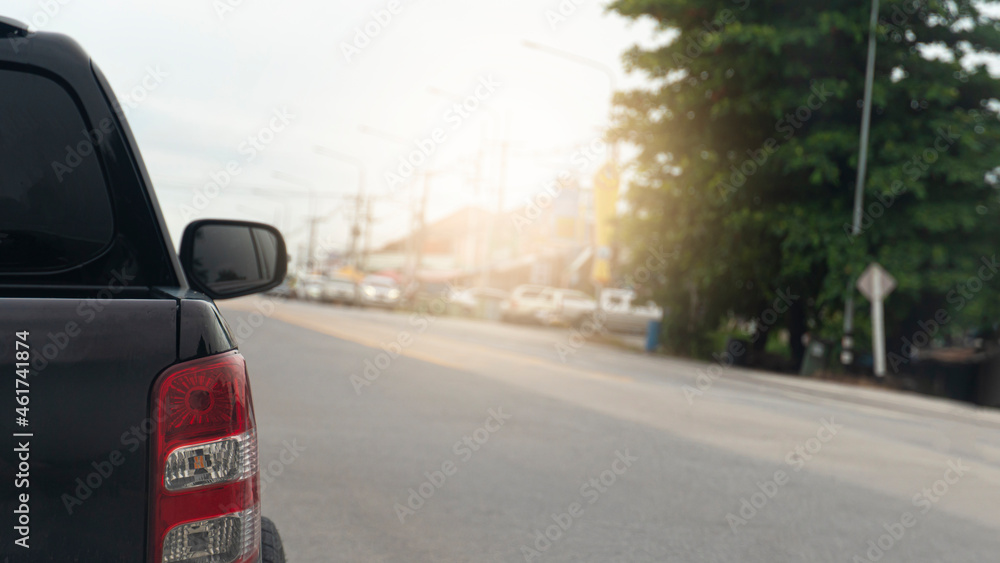 Rear side of pickup car black color on the asphalt road alone. The way to the destination or travel for tourism. Blurred background of a provincial city on the side of the road.