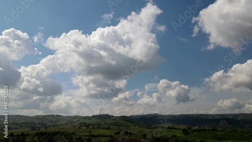bird's-eye view through the green forest Clouds and turquoise skies, in the background, are windmills spinning electric generators.