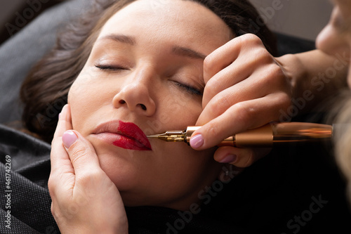 Young woman making lips tatouage in a dressing makeup room. Lips tatouage process .Woman making lips blushing. Make-up artist in beauty studio doing makeup for beautiful girl. Making mua.