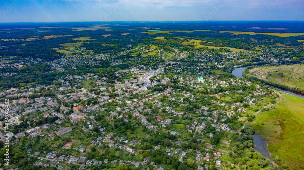 Aerial view of a small city on a beautiful summer day with a green landscape behind it. Picture from the drone of the village on a sunny day. Summer rural landscape from the top aerial view.