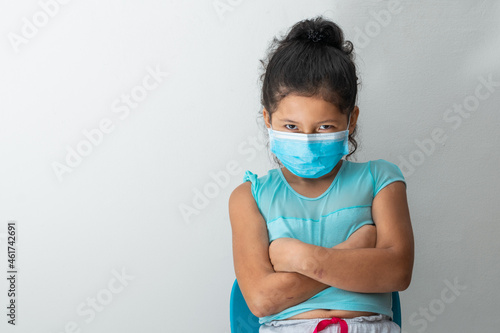 little girl looking into the camera with a malicious face  sitting with crossed arms and blue surgical mask. Medical  pharmaceutical and sanitary concept.