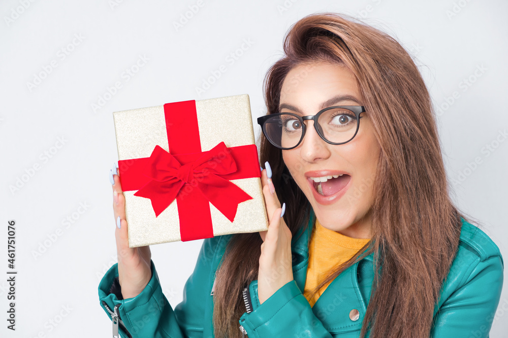 Amazed woman holding gift box - present with ribbon, wearing green leather jacket, isolated on white background. Pretty girl with a present at holiday Birthday, New Year, Valentine's Day Amazed woman holding gift box - present with ribbon, wearing green leather jacket, isolated on white background. Pretty girl with a present at holiday Birthday, New Year, Valentine's Day