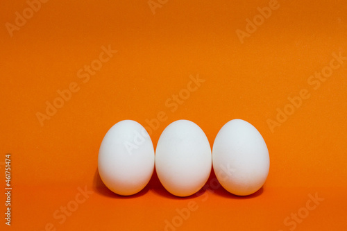 three white eggs on orange background