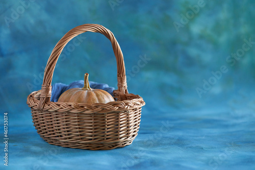  Pumpkin in a willow basket on a blue textured background with light gilding. Selective focus. Copy space.