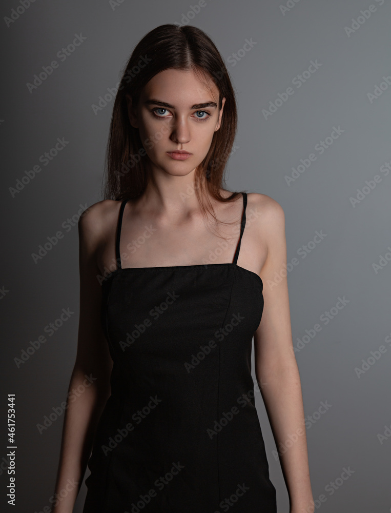 Fototapeta premium Beautiful woman with nude makeup and volume brown long hair looking mystery in black dress on grey background. Closeup. Art