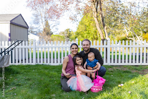 Happy young family in backyard with white fence and trees as background