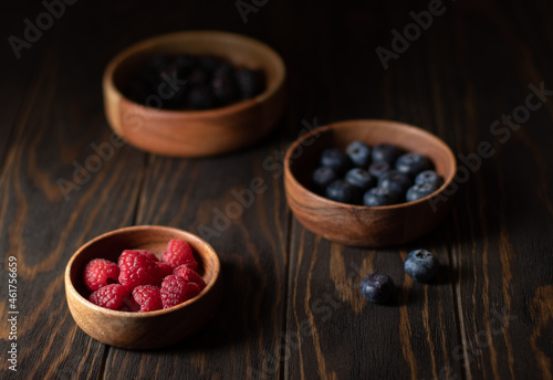 Fototapeta Naklejka Na Ścianę i Meble -  Berries of raspberries, blueberries and blackberries in wooden bowls on a dark background. Photo in a dark key