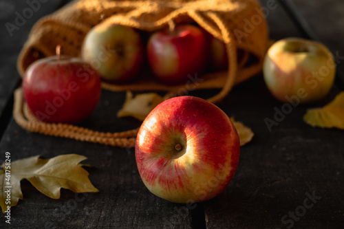 A fresh red apple close-up near a knitted bag on a wooden table in an apple orchard.