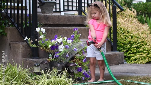 Toddler girl watering the garden on a summer day. Child playing with the water hose. Toddler summer fun activities photo
