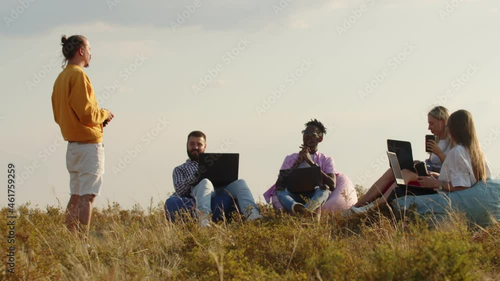 Field, four people are sitting in chair bags the grass with laptops their knees, listening to their coach. Concept of team building Field, four people are sitting in chair bags the grass with laptops their knees, listening to their coach. Concept of team building