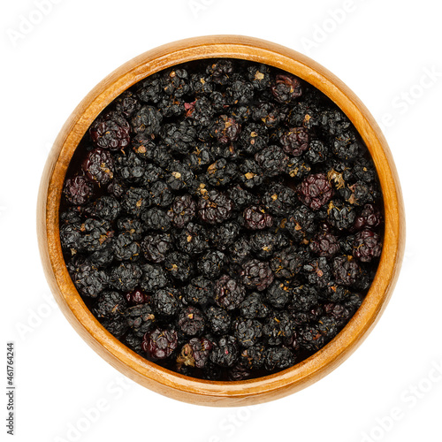 Dried ripe European blackberries in a wooden bowl. Air dried wild brambles, Rubus fruticosus, a sweet fruit, used for tea additive. Close-up from above, isolated on white background, macro food photo.
