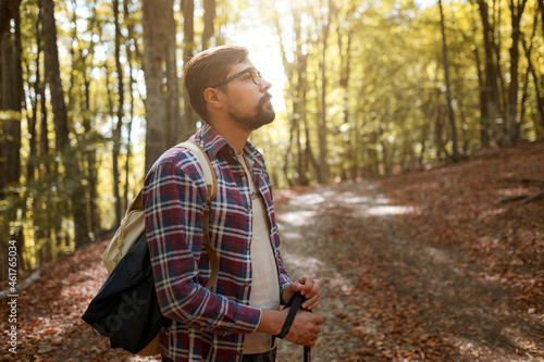Caucasian hipster male model outdoors in nature. Colorful landscape with trees, rural road, orange and red leaves, sun in autumn.