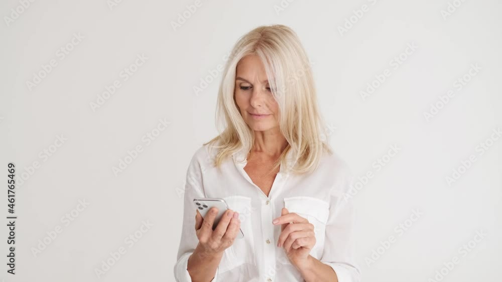Positive mature woman looking at the phone in the white studio Positive mature woman looking at the phone in the white studio