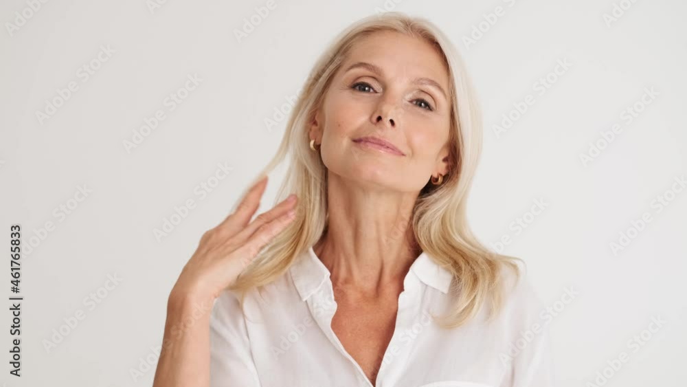 Close-up view of the smiling mature woman correcting her appearance in the white studio Close-up view of the smiling mature woman correcting her appearance in the white studio