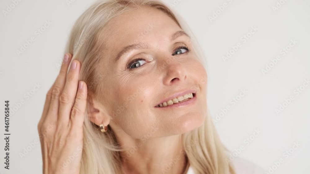 Close-up view of the happy mature woman correcting her appearance at the camera in the white studio Close-up view of the happy mature woman correcting her appearance at the camera in the white studio