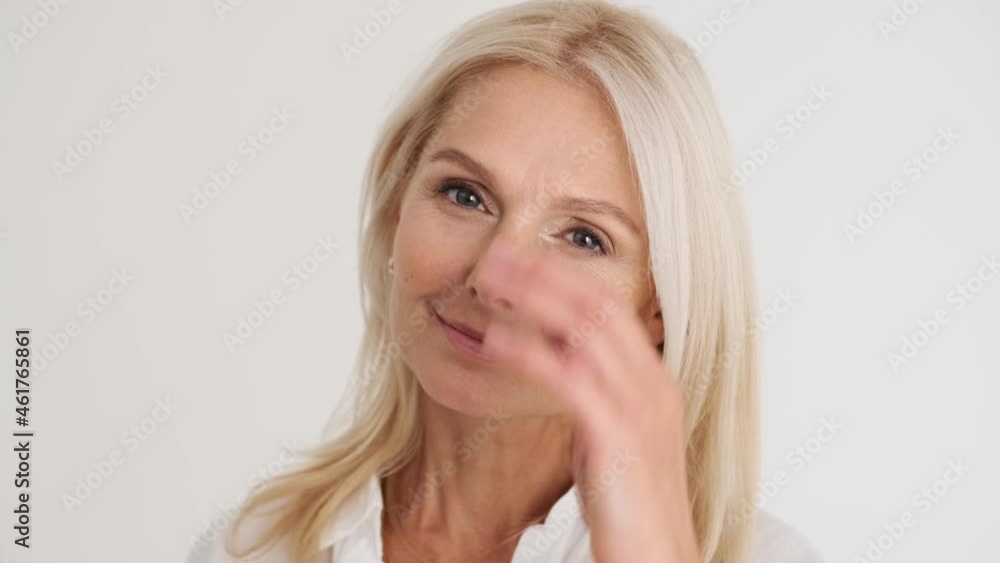 Close-up view of the smiling mature woman correcting her hairstyle at the camera in the white studio