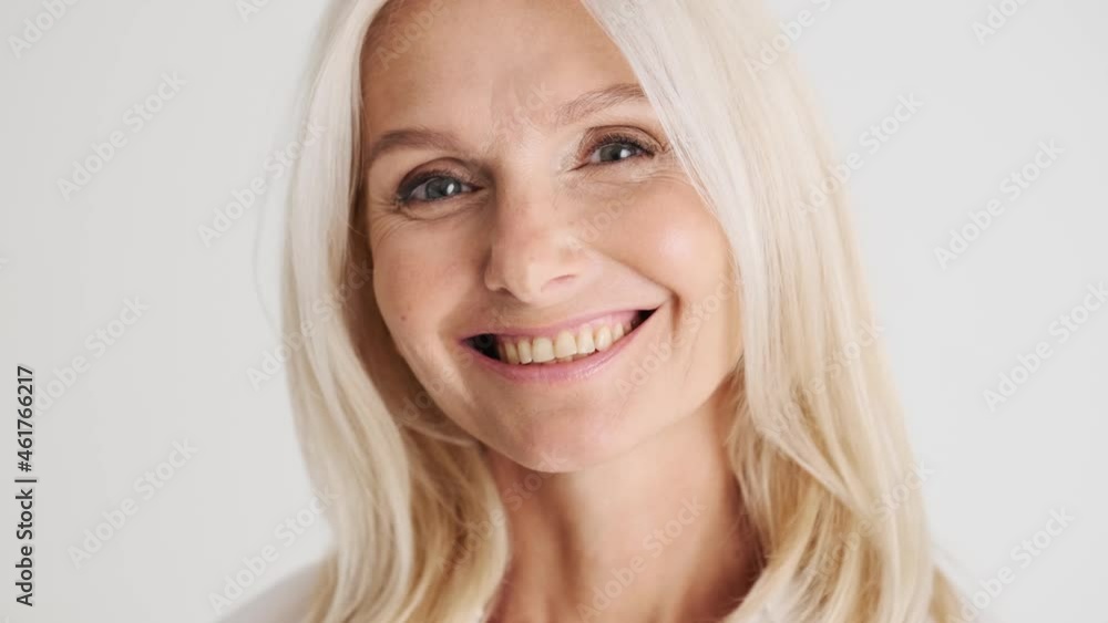 Close-up view of the handsome smiling mature woman looking at the camera in the white studio Close-up view of the handsome smiling mature woman looking at the camera in the white studio