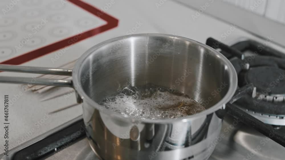 A chef in white kitchen making sugar syrup in a saucepan A chef in white kitchen making sugar syrup in a saucepan