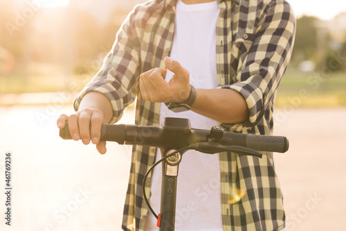 Unrecognizable tourist man take electric kick scooter or bike bicycle in sharing parking lot, smart watch application. Eco transportation. Smartwatch phone app for scooter