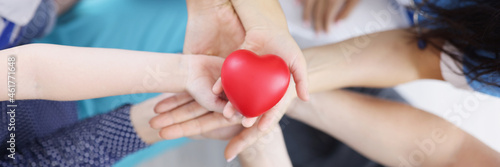 Many adults and children hands are holding plastic toy heart top view