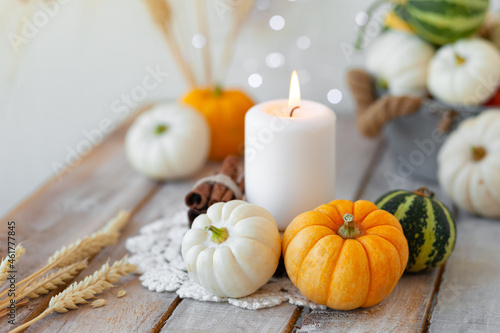 Pumpkins and candle with fairy lights around on a wooden table. Autumn season image, cozy home atmosphere. Close up