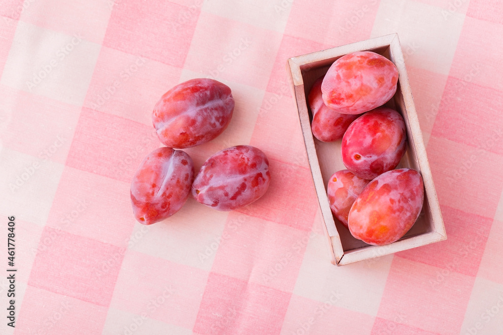 Fresh organic purple plums on a pink textile background. Ripe fruit with a wooden container on the tablecloth