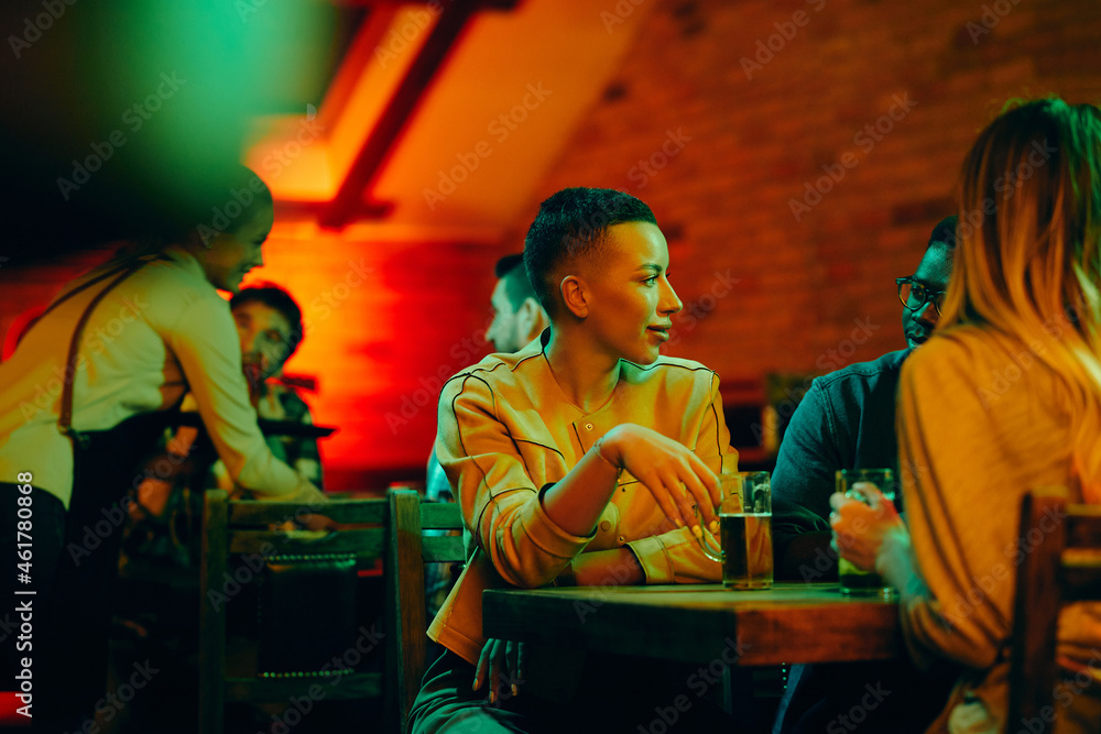 Young black woman and her friends enjoy in conversation while drinking beer in bar.