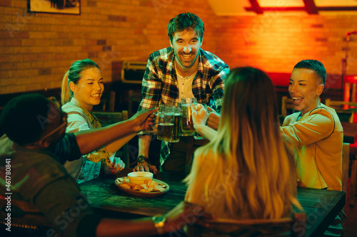 Young happy people toast with beer and and have fun while gathering in pub.