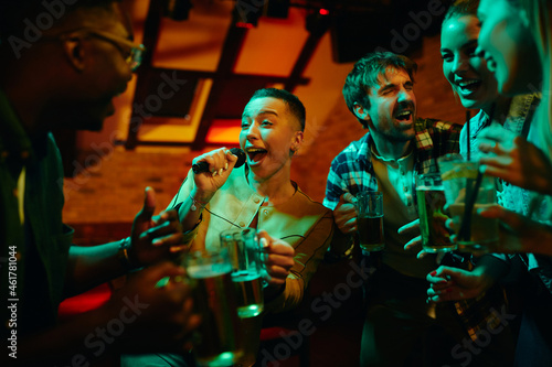 Group of carefree friends sing and have fun on night karaoke party in bar.