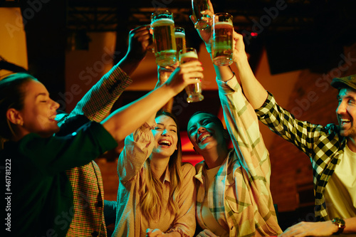 Group of young happy adults celebrate their friendship and toast with beer in bar.