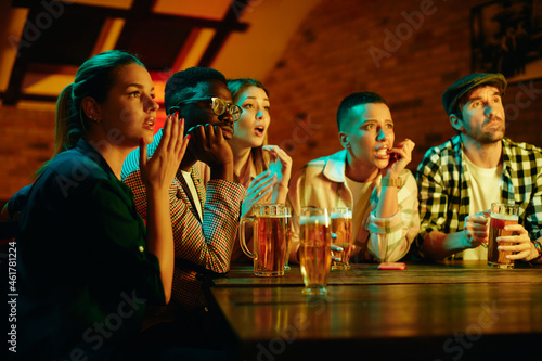Multi-ethnic group of friends watch sports match with anticipation while drinking beer in pub. photo