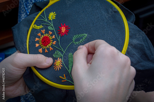 Women's hand embroidery in a hoop, a woman embroider a pattern on dark material. Close-up. The concept of needlework, hobby, leisure.