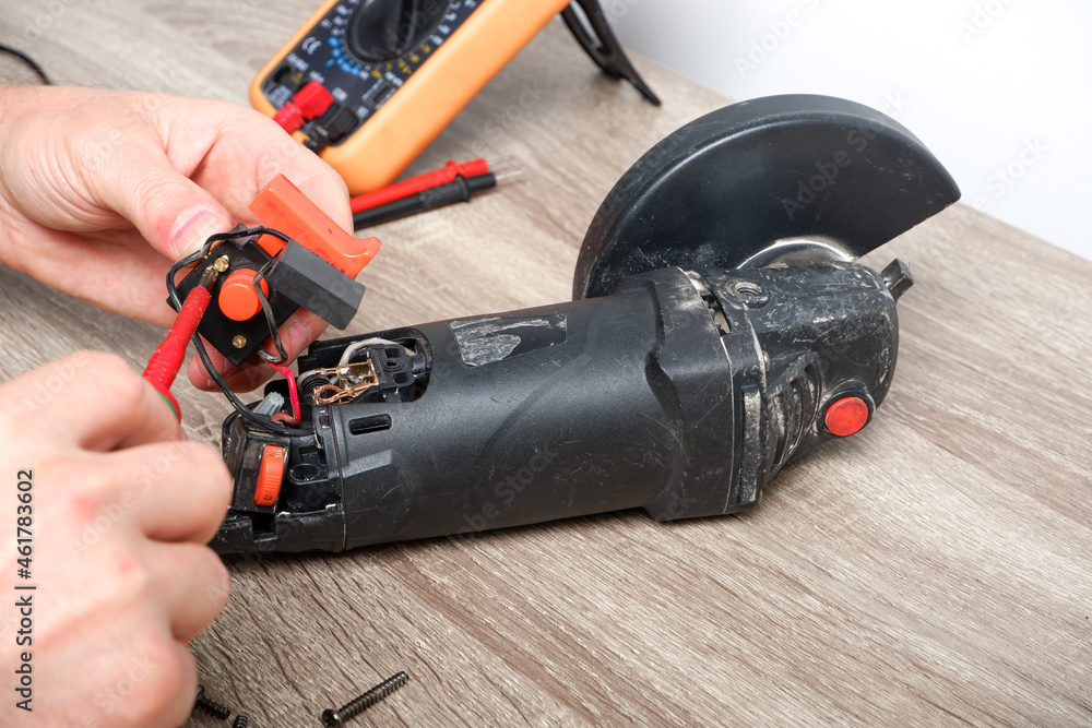 Power tool repair. A man repairs an angle grinder. Screwdriver, multimeter. Details of electrical appliance Power tool repair. A man repairs an angle grinder. Screwdriver, multimeter. Details of electrical appliance