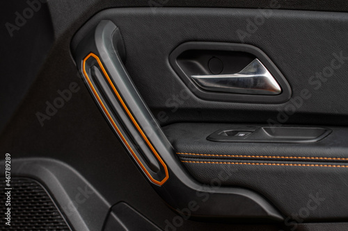 Car door handle with power window control. Dark leather interior of modern car. Dark black and orange car leather pleats stitch. Details of door handle with windows controls. Car window controls.