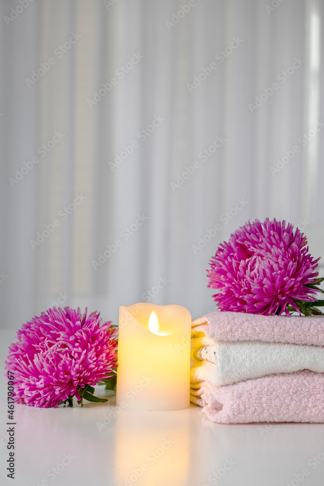 Set of fresh towels of pink and white color with purple aster flowers and candle on white table. Hotel spa and wellness concept. Copy space. Set of fresh towels of pink and white color with purple aster flowers and candle on white table. Hotel spa and wellness concept. Copy space.