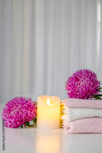 Set of fresh towels of pink and white color with purple aster flowers and candle on white table. Hotel spa and wellness concept. Copy space.