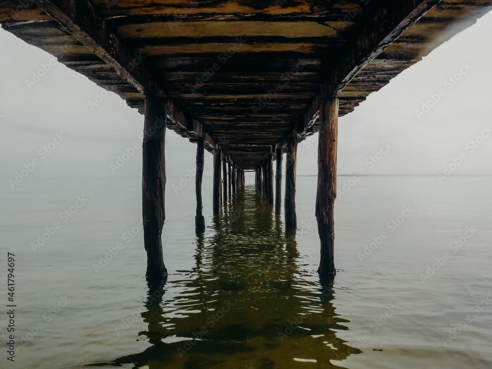 Symmetrical view underneath a wooden pier with still water Symmetrical view underneath a wooden pier with still water