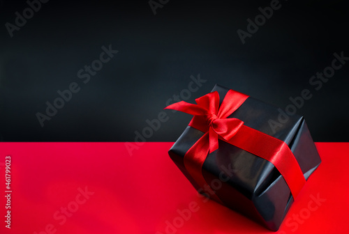 Black gift box with red bow on red and black background