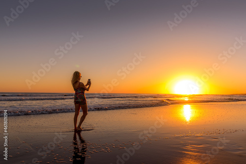 Woman on the beach photographing the sunset