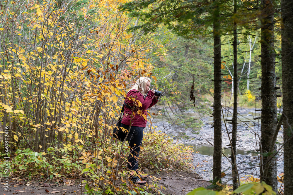 Naklejka premium Blonde woman photographer takes photos at Grand Portage State Park in Minnesota during fall