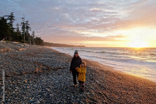 A mother and daughter posing for a photo on agate beach with the waves crashing to shore and the sun setting, on a beautiful evening on Agate Beach, Haida Gwaii, British Columbia, Canada photo