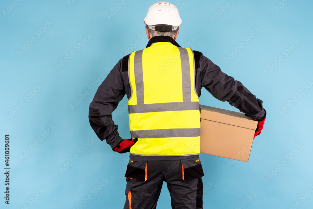 warehouse worker with his back to camera. Man in a yellow vest and helmet. warehouse worker with a box in his hands. Concept is a warehouse worker career. Distribution company employee. warehouse worker with his back to camera. Man in a yellow vest and helmet. warehouse worker with a box in his hands. Concept is a warehouse worker career. Distribution company employee.