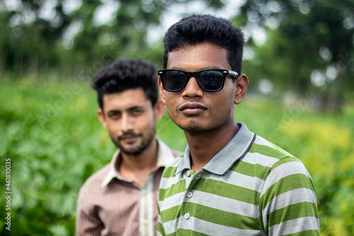 Two handsome boys are standing in the middle of green nature and one of them is wearing sunglasses. the background blur.