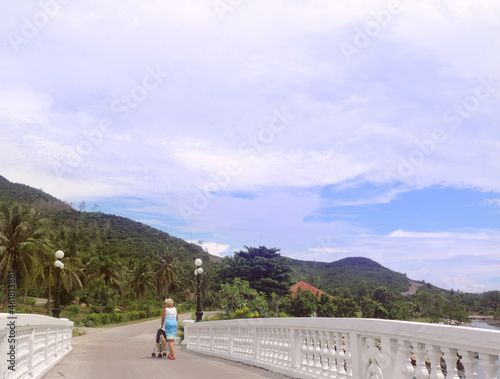 Mother with baby in stroller walking in green tropical park, happy relaxing family outdoors