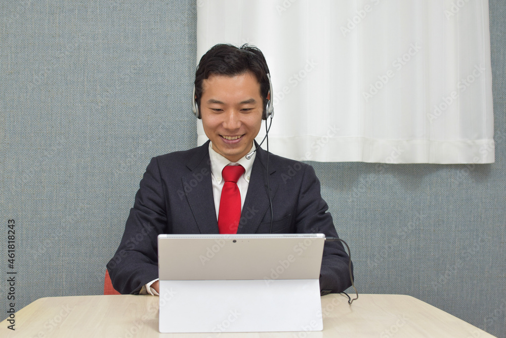 A young Asian man with a headset wearing business suit talks on video meeting app with clients and makes a smile A young Asian man with a headset wearing business suit talks on video meeting app with clients and makes a smile