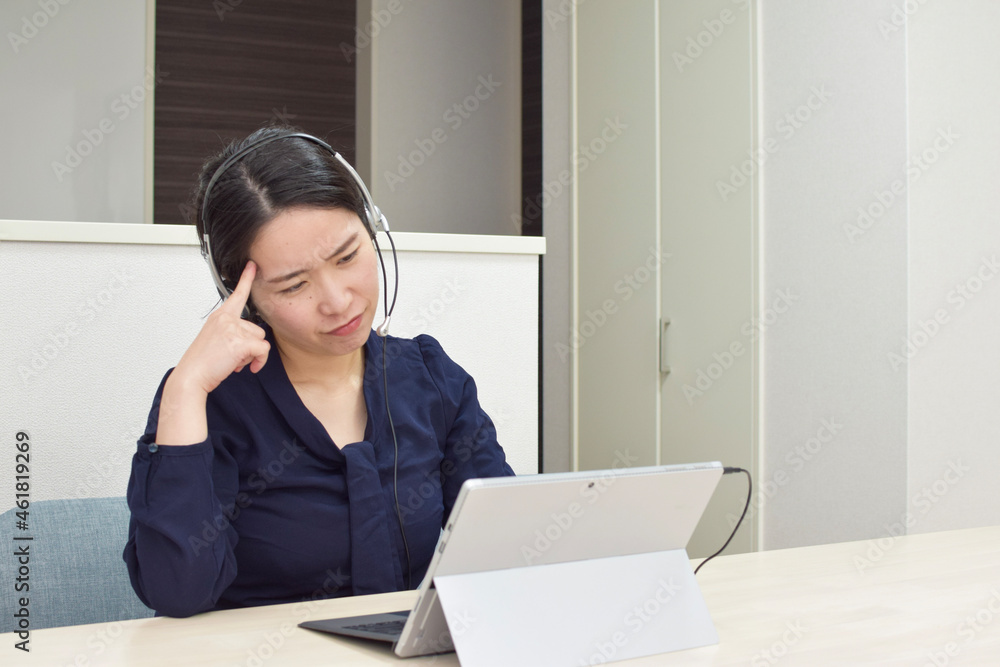 A young Asian woman wearing a headset thinks about how to deal with her customer during telework at home A young Asian woman wearing a headset thinks about how to deal with her customer during telework at home